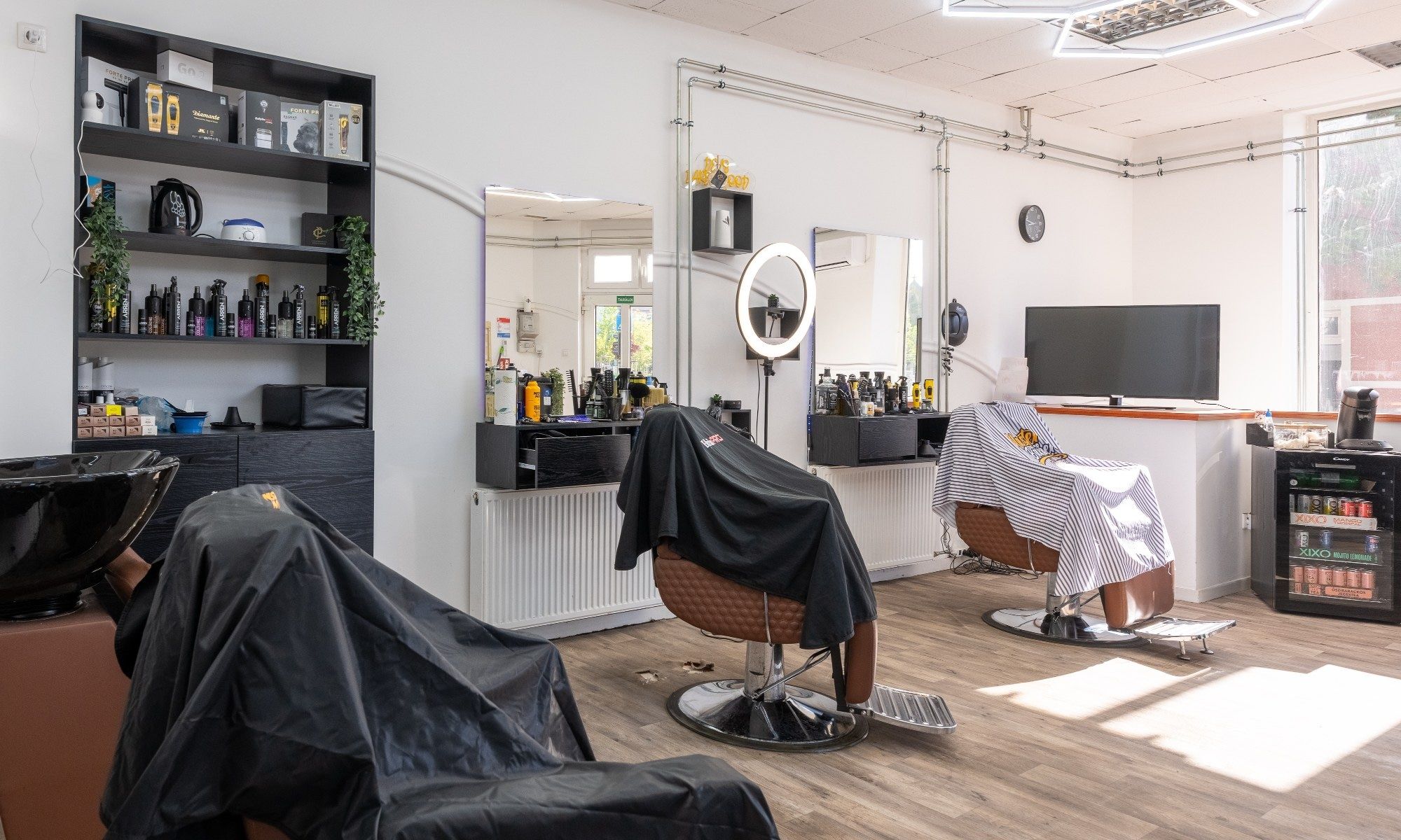 Barberszékek közelről, a háttérben polc hajápolási termékekkel és körlámpa.